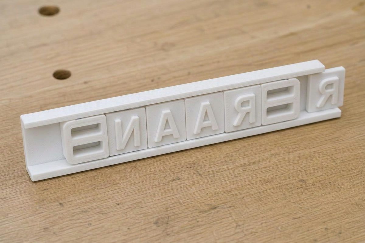 A short word seated in the white C-channel holder rail, one letter tile half slid into the open end, with a ladder-style end clip pushed in at each end